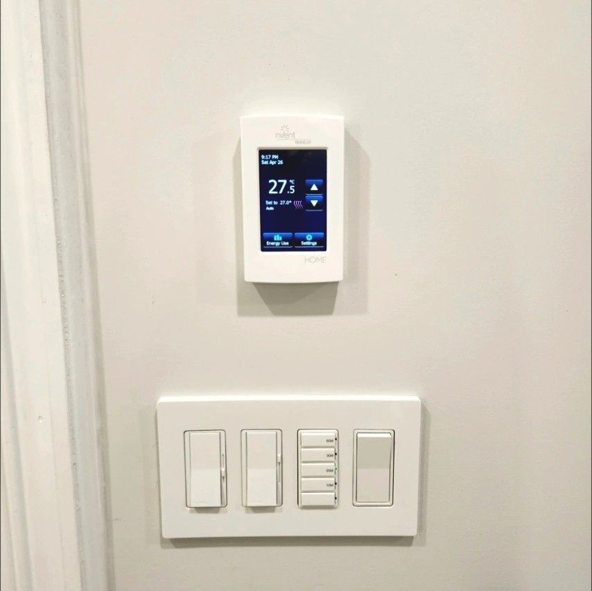 Touchscreen floor heat thermostat above a four-gang dimmer and switch plate