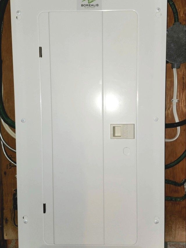 New white electrical panel with a Borealis Electric sticker on a plywood backboard